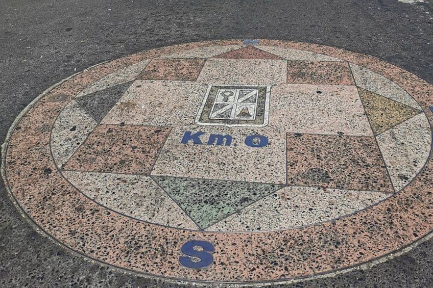 A circular manhole cover with a geometric pattern and the text 'Km 0' on it. 3