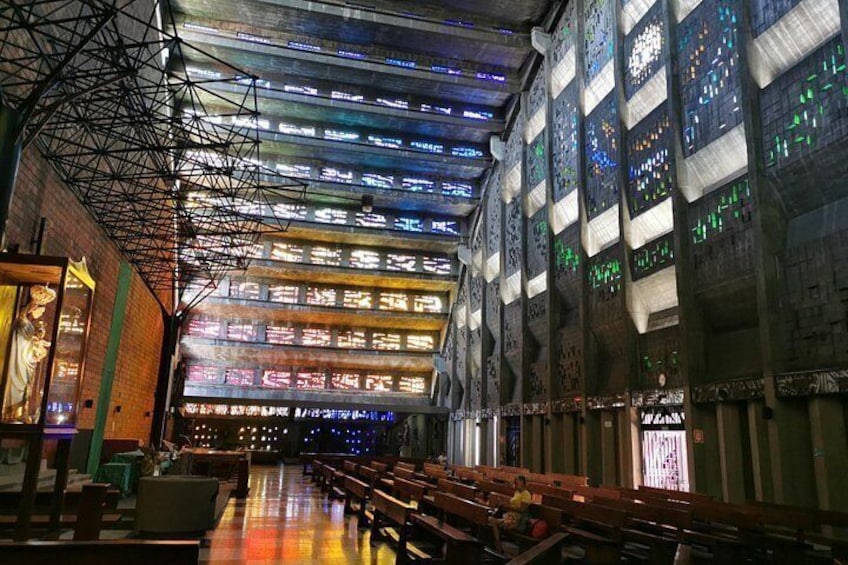 An interior with a high ceiling, stained glass windows, and rows of wooden benches. 4