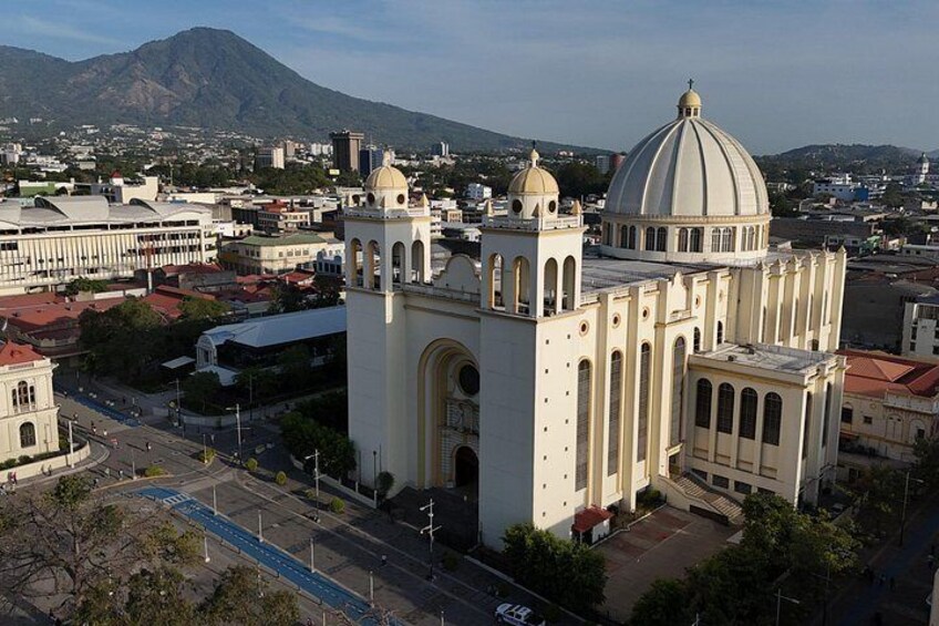 A large white church with a dome and bell tower, surrounded by urban buildings and a mountain in the background. 2