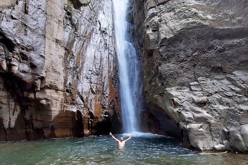 A waterfall, rocky cliffs, and a person in the water. 1