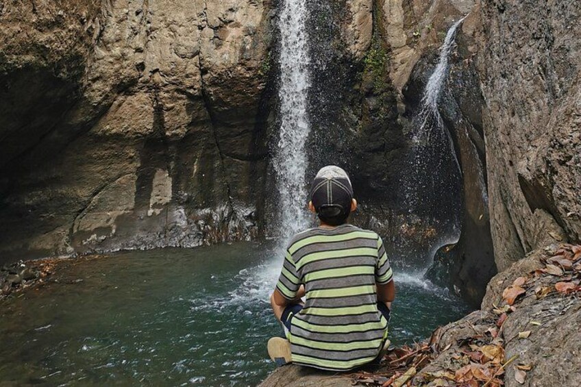 A person sitting by a waterfall in a rocky area. 2