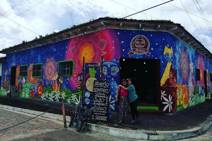 A colorful mural on a building with a bicycle and people standing in front. 1
