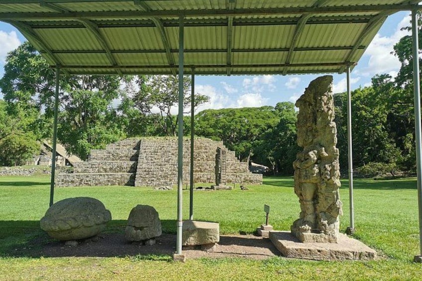 A stone structure under a shelter, surrounded by grass and trees. 2