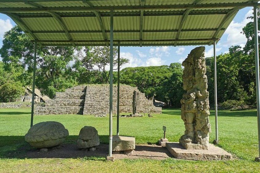 A stone structure under a shelter, surrounded by grass and trees. 2