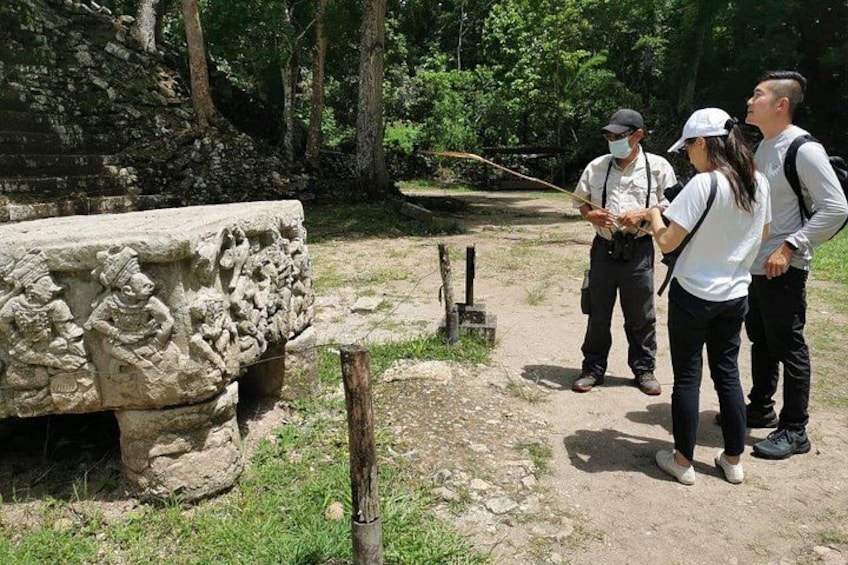 A stone carving, a wooden post, and a group of people observing. 4