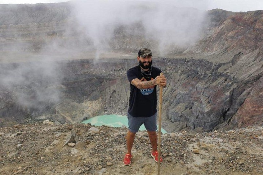 Una persona de pie en un terreno rocoso con una salida de vapor, vestida con camiseta negra, pantalones cortos y zapatos rojos. 3