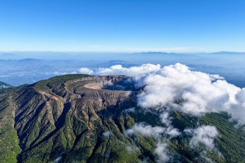 Un cráter volcánico rodeado de montañas cubiertas de exuberante vegetación y nubes. 4
