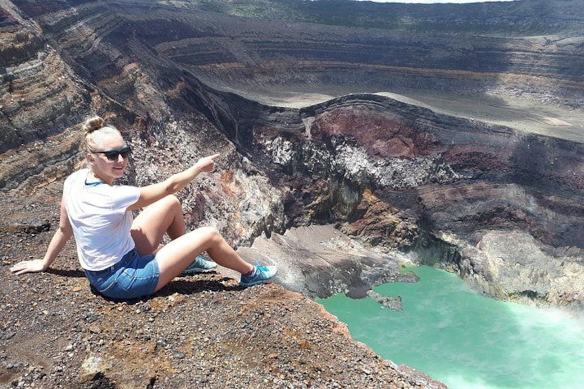 Una persona sentada sobre un saliente rocoso, con vistas a una piscina turquesa y un paisaje volcánico al fondo. 4