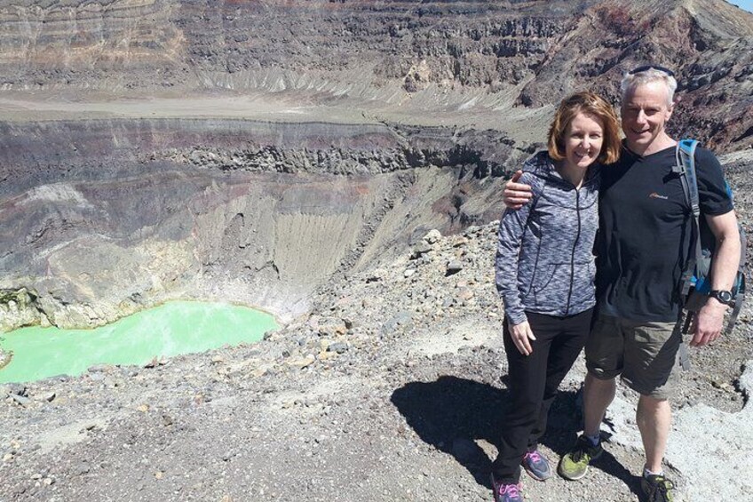 Two people standing on a rocky terrain with a greenish pond and a barren landscape in the background. 4
