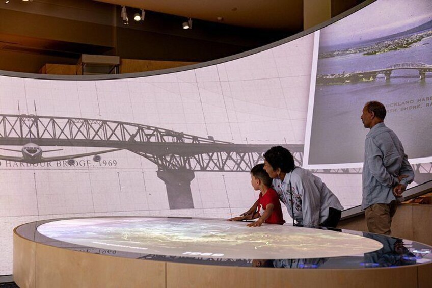 A large circular display with a bridge model, a projection screen, and a person standing to the side. 3