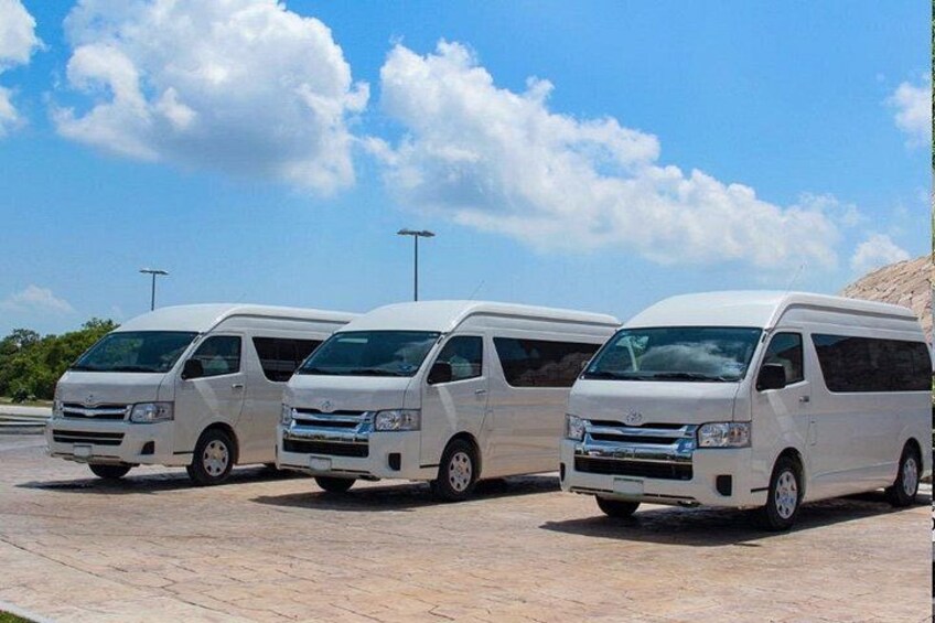 Tres camionetas blancas estacionadas en fila sobre una superficie pavimentada, con cielo despejado y nubes al fondo. 3