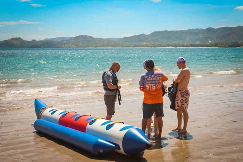 A beach with a blue and white inflatable raft, a person in a life jacket, and another in an orange shirt with a number on the back. 4