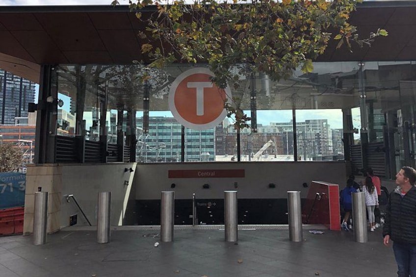 Entrée de la station T Central, avec un grand panneau en forme de T, des fenêtres en verre et des potelets. 4