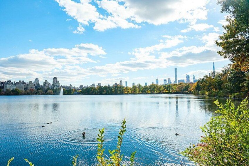 Un lac avec la silhouette d’une ville en arrière-plan, une fontaine et quelques éléments de végétation au premier plan. 2