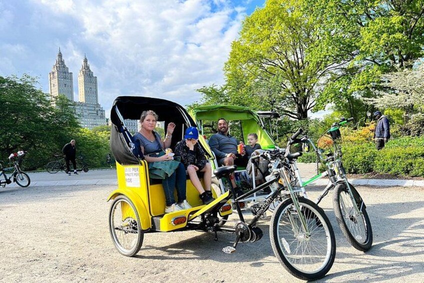 Un pousse-pousse jaune avec des passagers, un vélo, et une vue sur la ville avec de grands immeubles en arrière-plan. 3