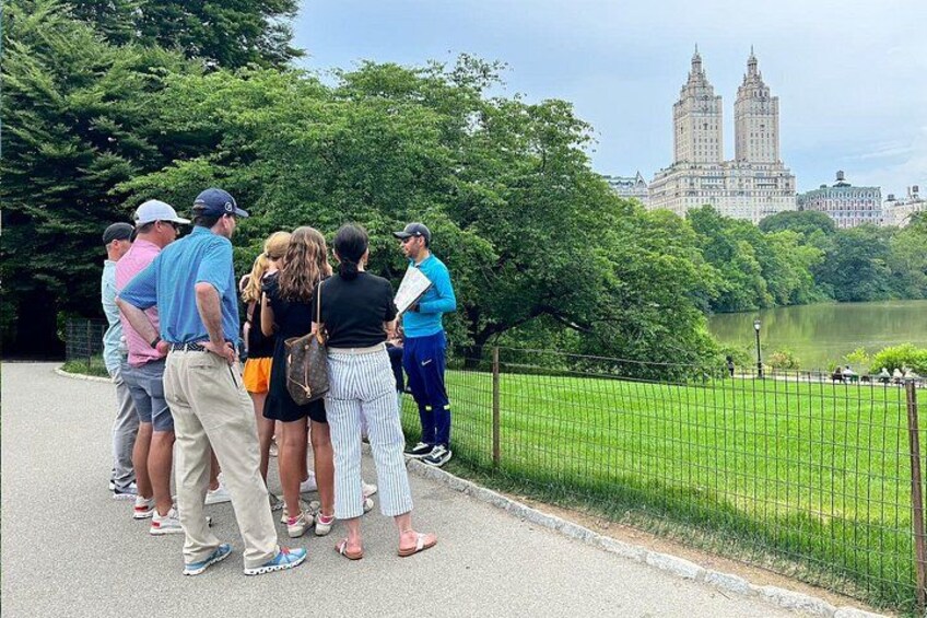 Un groupe de personnes se tient sur un sentier, près d’un lac, avec un grand bâtiment en arrière-plan. 4