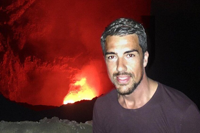 A person standing in front of a volcanic landscape with visible lava flow. 1
