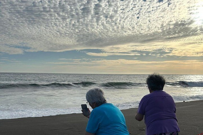 Deux personnes se tiennent sur une plage, l’une d’elles tient un téléphone intelligent, avec des vagues en arrière-plan et un ciel nuageux. 3