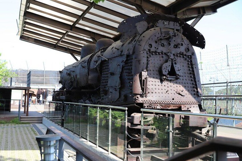 A large, rusted train engine with a metal roof, surrounded by a fence and a glass barrier. 4