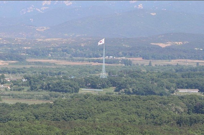 A flag atop a tower, surrounded by a hilly landscape with scattered buildings. 2