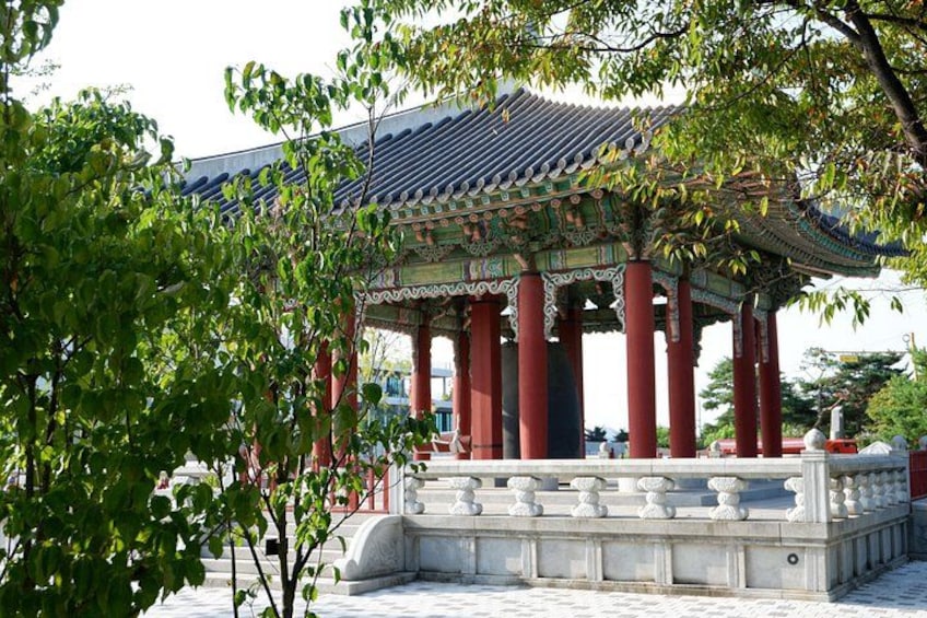 A traditional Korean pavilion with ornate roof and red pillars, surrounded by lush greenery. 2