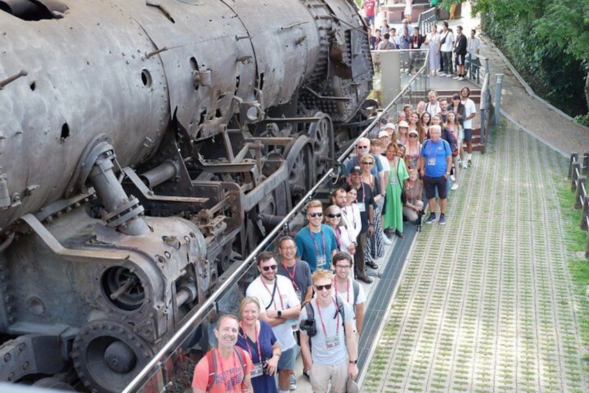 A group of people standing on a bridge next to a large, rusted train engine. 2