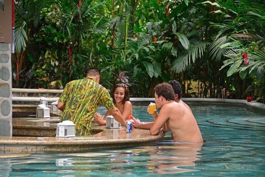 Une piscine où des personnes sont assises sur les marches, entourée d’une végétation luxuriante. 3