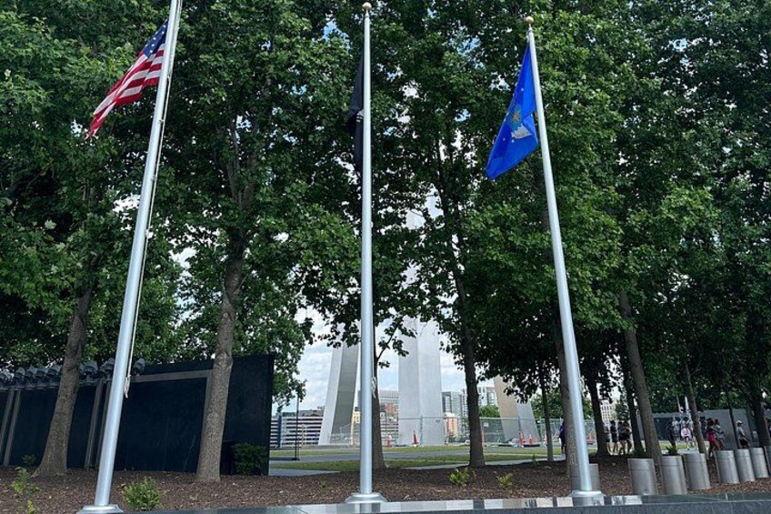 Three flagpoles with flags, trees, and a building in the background. 3