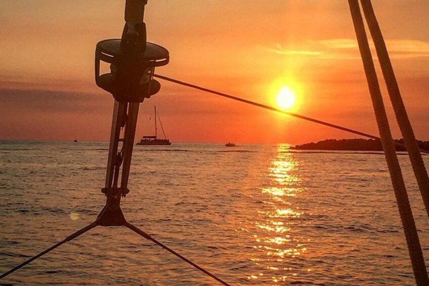 A sunset over the ocean with a sailboat and a distant landmass. 2