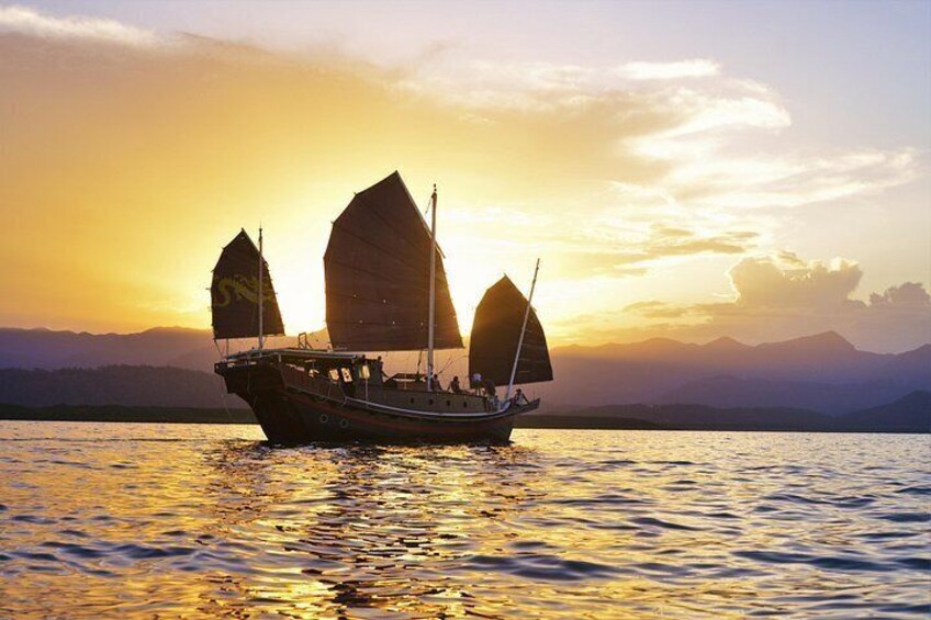 Een traditionele zeilboot met meerdere zeilen op kalm water tijdens zonsondergang. 5