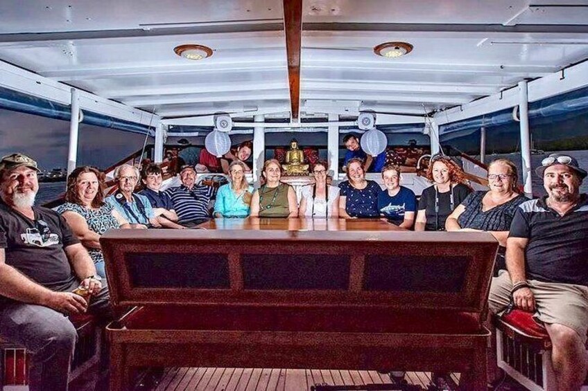 Een groep mensen zit rond een houten tafel op een boot. 2