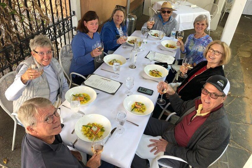 Un groupe de personnes est assis autour d’une table, devant des assiettes remplies de nourriture et des verres de vin. 5