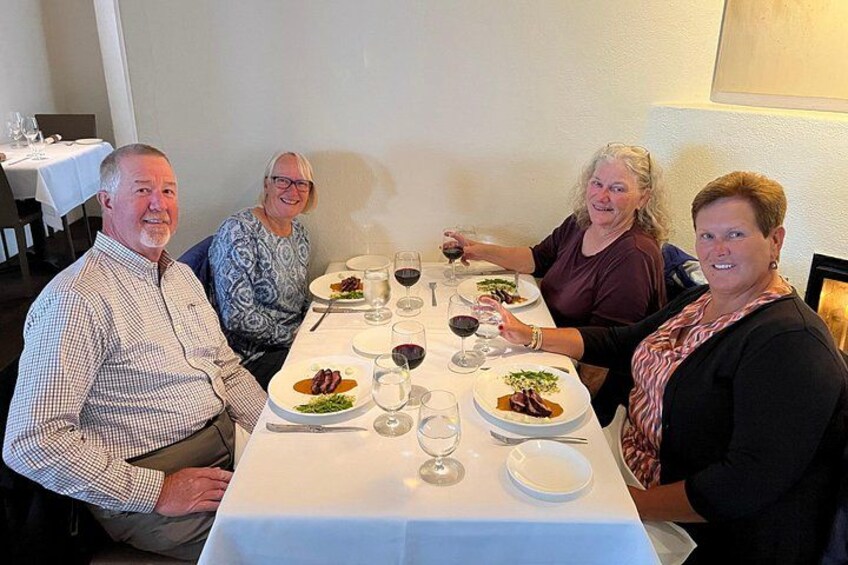 Un groupe de personnes est assis autour d’une table, devant des assiettes remplies de nourriture et des verres de vin. 1