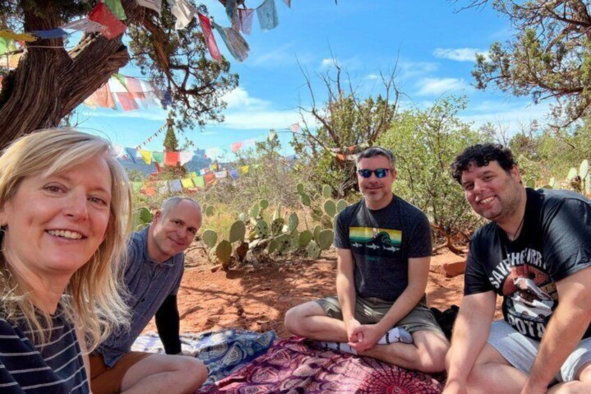 Three people sitting on a blanket under a tree with colorful flags in a desert landscape. 4