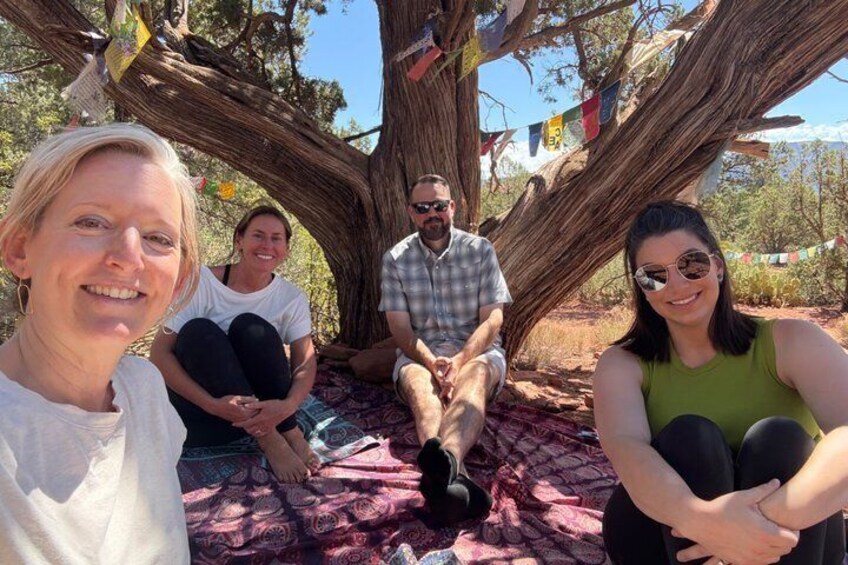 A group of people sitting under a large tree with colorful flags. 3