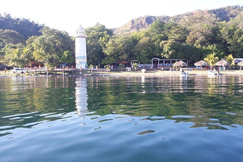 A calm lake with a lighthouse, trees, and a few people on the shore. 4