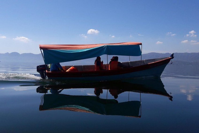 A boat with a blue canopy on calm water, reflecting the boat and surroundings. 3