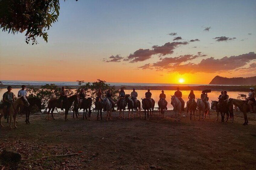 A sunset over a body of water with people on horseback. 4