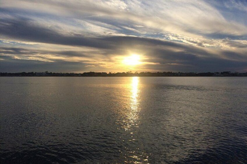 Een zonsondergang boven een rustig wateroppervlak, met een stadsachtergrond. 5