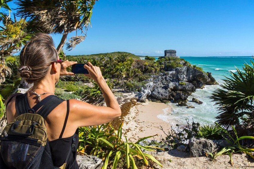 A person taking a photo of a beach with rocky outcrops and a clear blue sky. 3