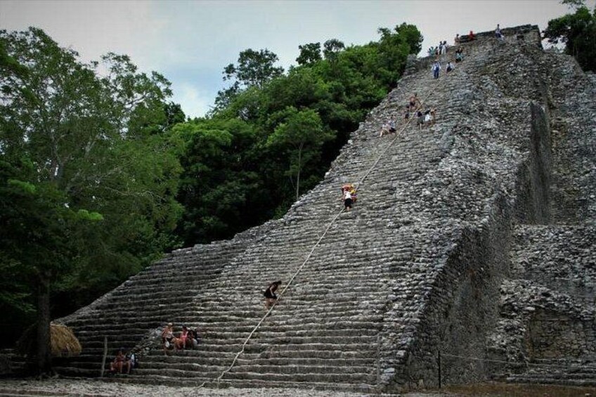 A large stone pyramid with people climbing its steps. 5