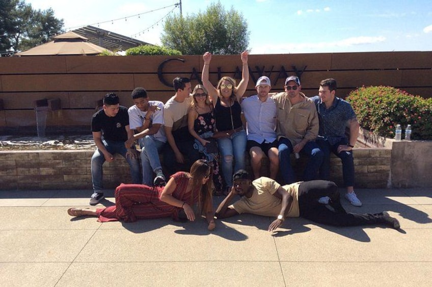 A group of people sitting and standing in front of a building with a sign. 3