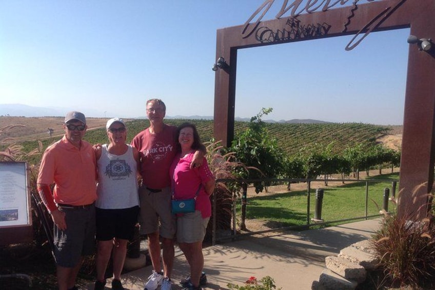 A group of people standing in front of a sign with a vineyard in the background. 5