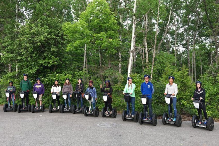 Eine Gruppe von Personen auf Segways steht in einer Parkbucht mit Bäumen im Hintergrund. 3