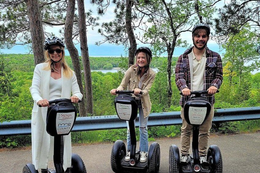 Three people on Segways in a natural setting with trees and a view of the ocean. 4