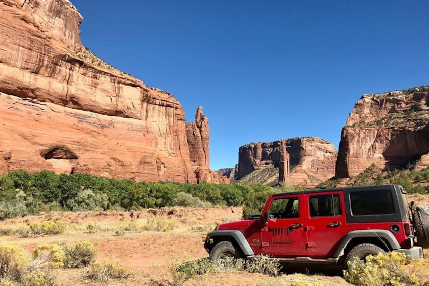 Un Jeep rojo estacionado en un paisaje desértico con formaciones rocosas rojas al fondo. 3