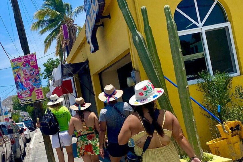 A group of people walking on a street, a yellow building, and a cactus. 5