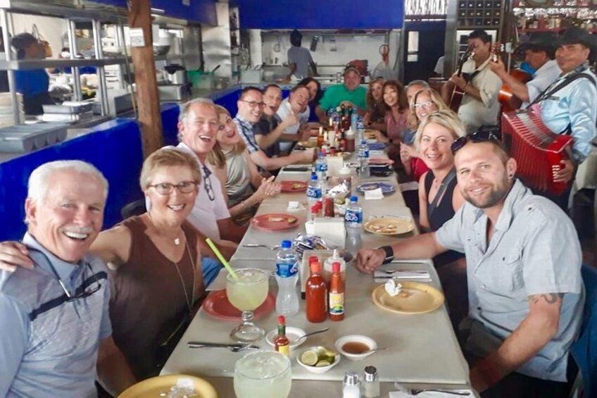 Un grupo de personas sentadas en una mesa larga en un restaurante, con varios platos y bebidas. 3