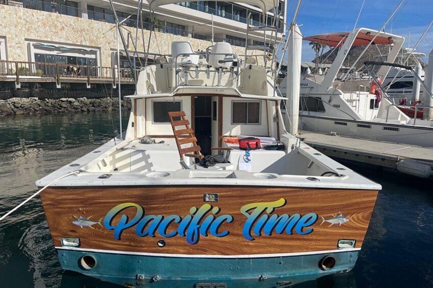 Un barco de madera llamado 'Pacific Time' atracado en un puerto deportivo, con otros barcos y un edificio al fondo. 3