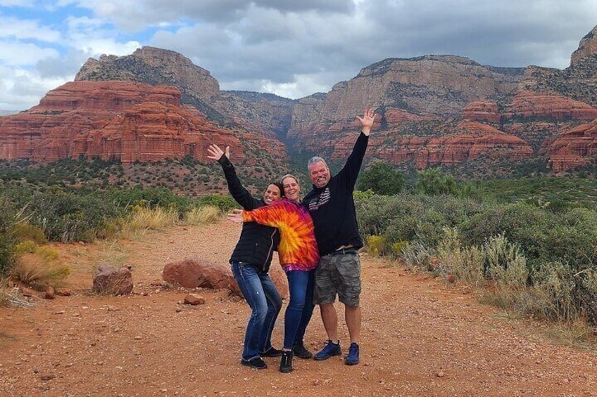 Three people standing on a dirt path with red rock formations in the background. 4